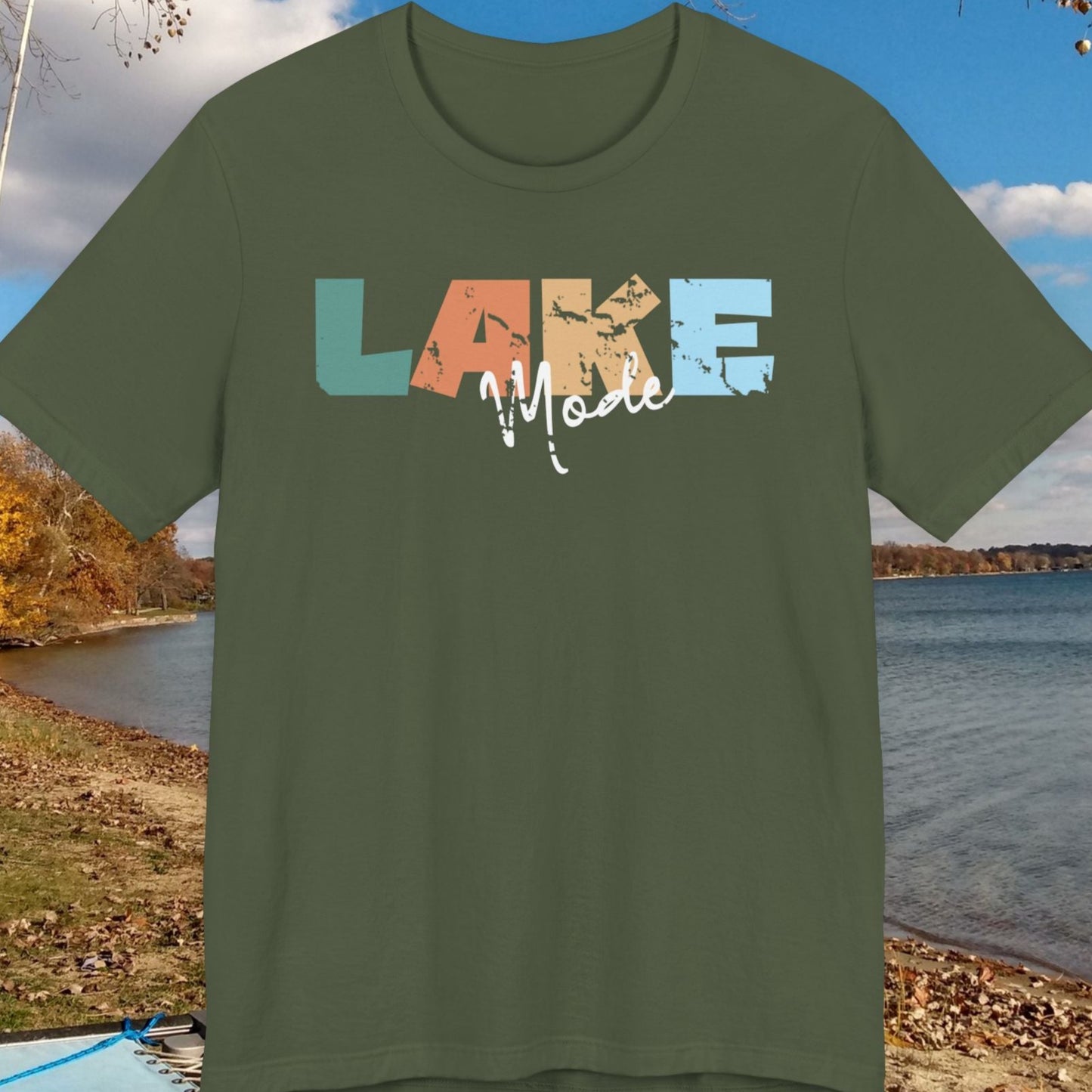 Green t-shirt with 'LAKE' text in colorful letters on a scenic lakeside background