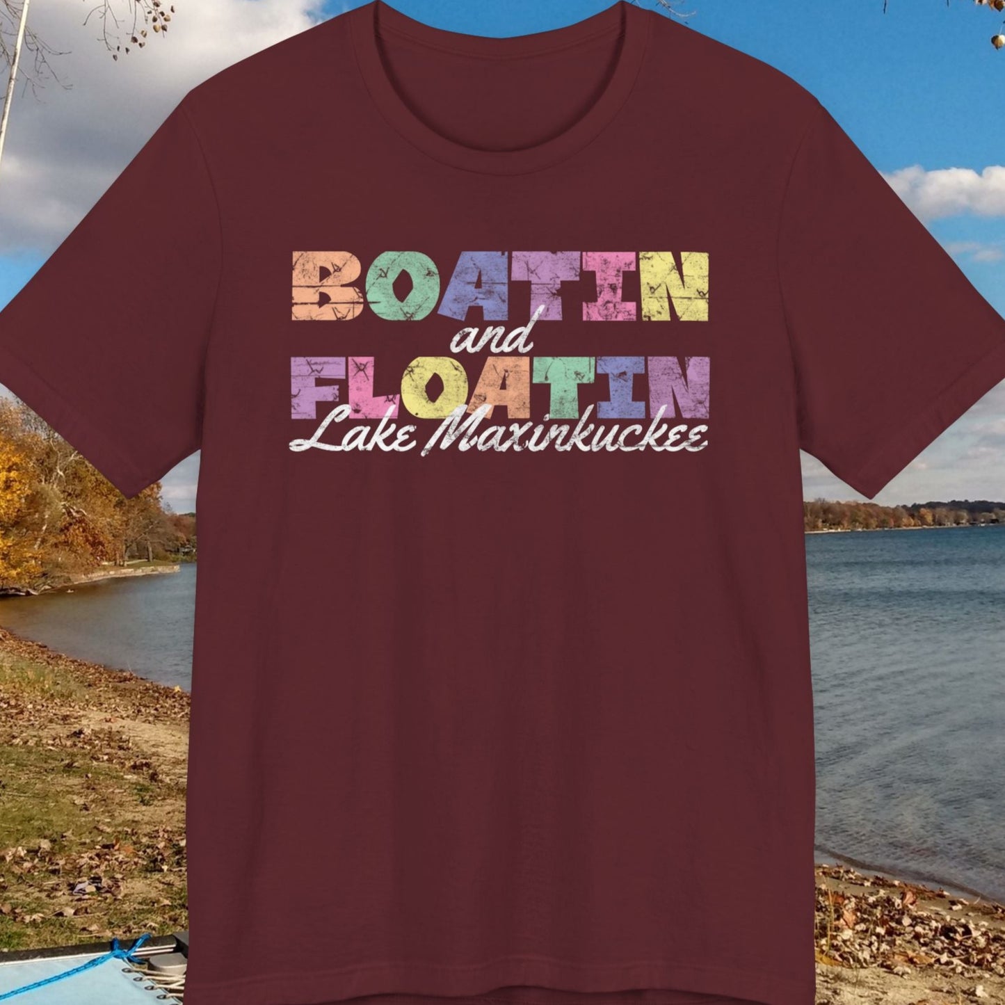 Maroon t-shirt with colorful BOATIN AND FLOATIN LAKE MAXINKUCKEE text on a lake shore background