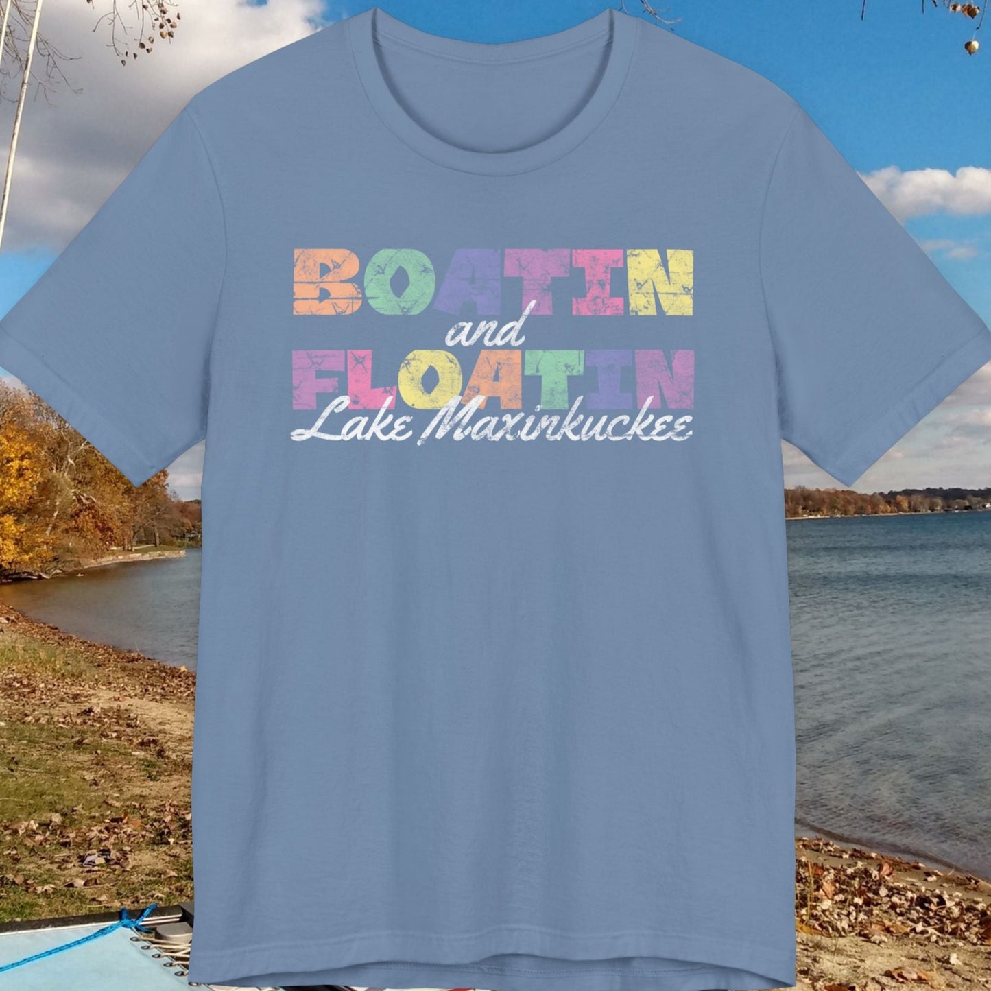 Blue t-shirt with colorful BOATIN AND FLOATIN LAKE MAXINKUCKEE text on a lake shore background