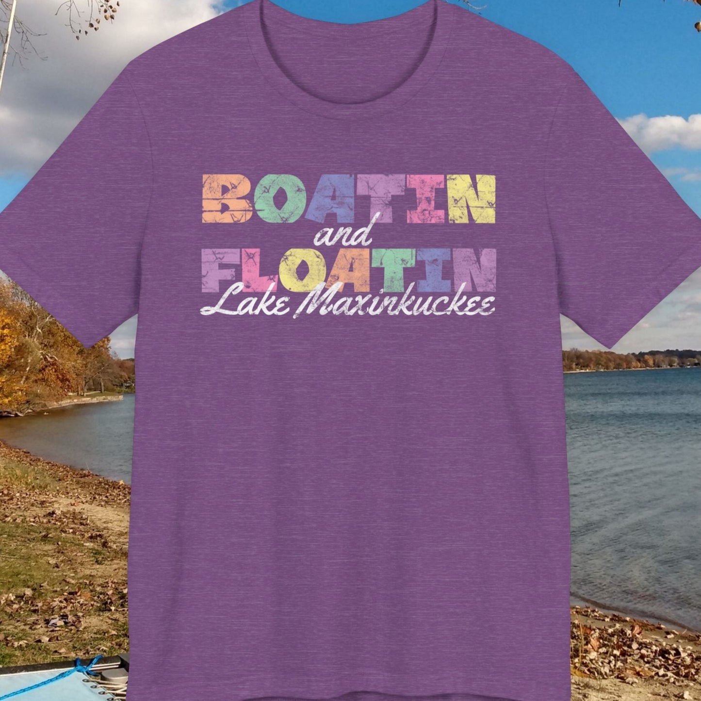 Purple t-shirt with colorful BOATIN AND FLOATIN LAKE MAXINKUCKEE text on a lake shore background