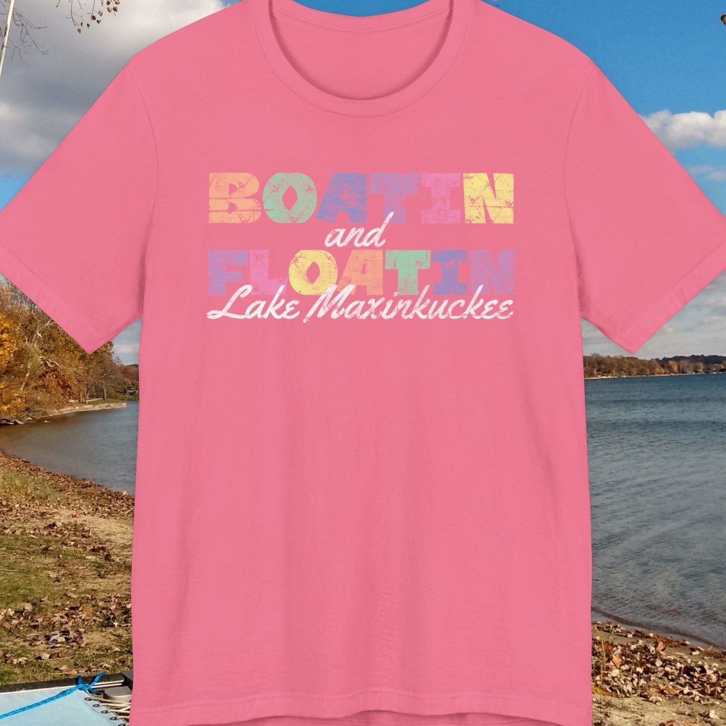 Pink t-shirt with colorful BOATIN AND FLOATIN LAKE MAXINKUCKEE text on a lake shore background