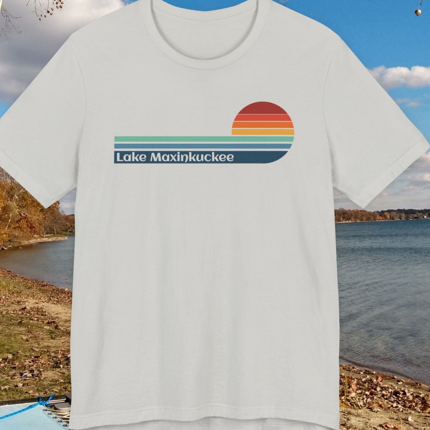 White t-shirt with 'Lake Maxinkuckee' design on a background of a lake and trees.