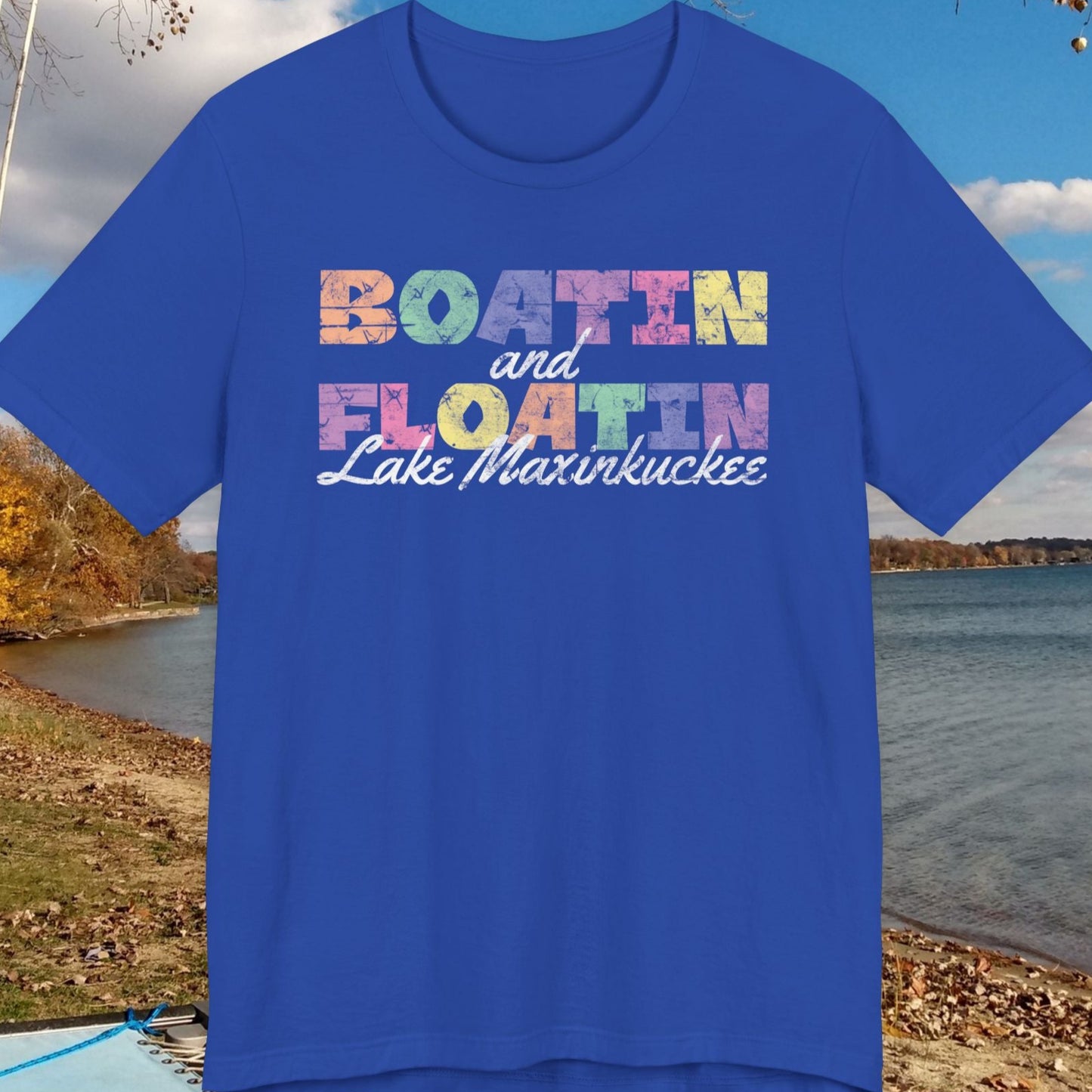 Blue t-shirt with colorful BOATIN AND FLOATIN LAKE MAXINKUCKEE text on a lake shore background