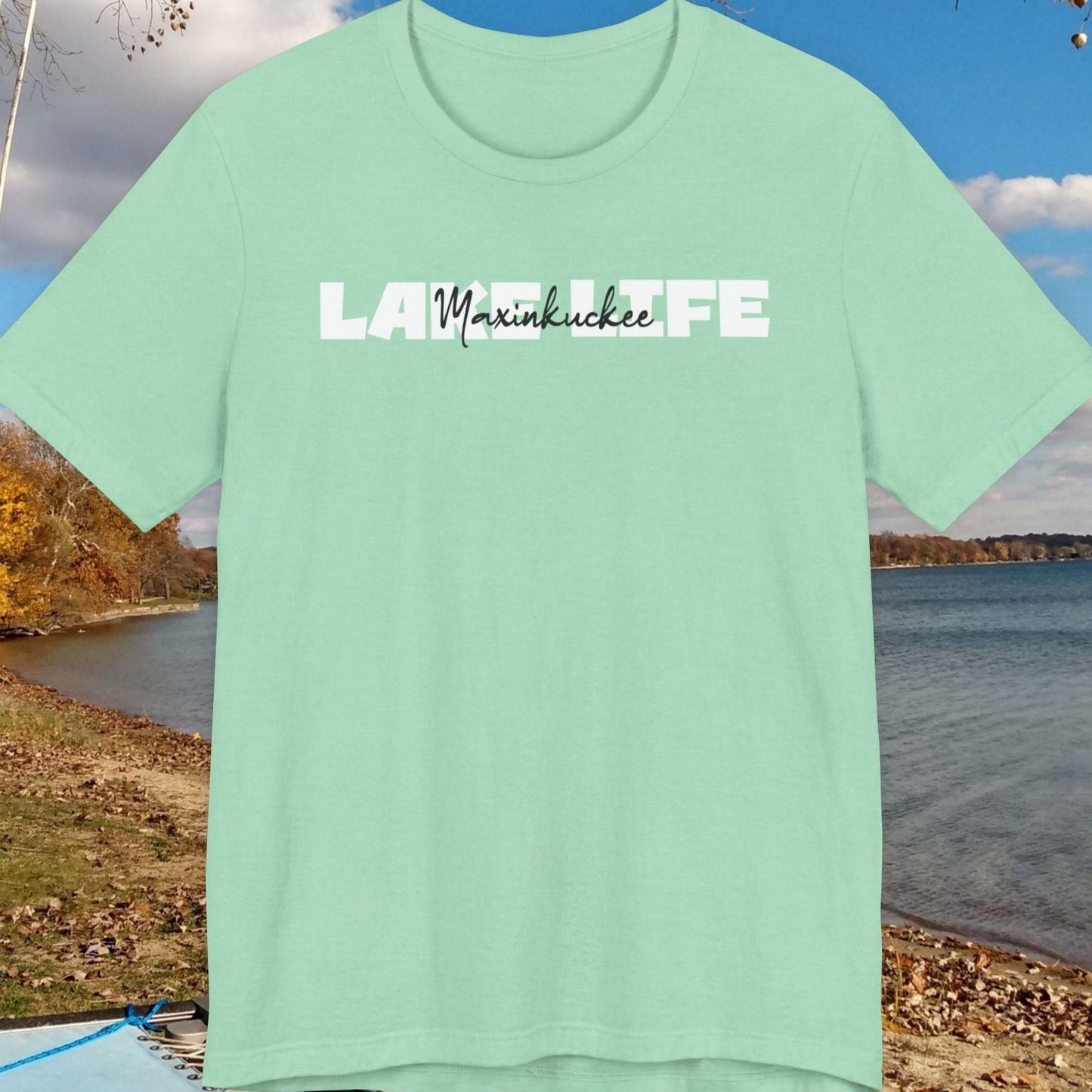 Mint green t-shirt with 'Lake Maxinkuckee' text against a scenic lake background