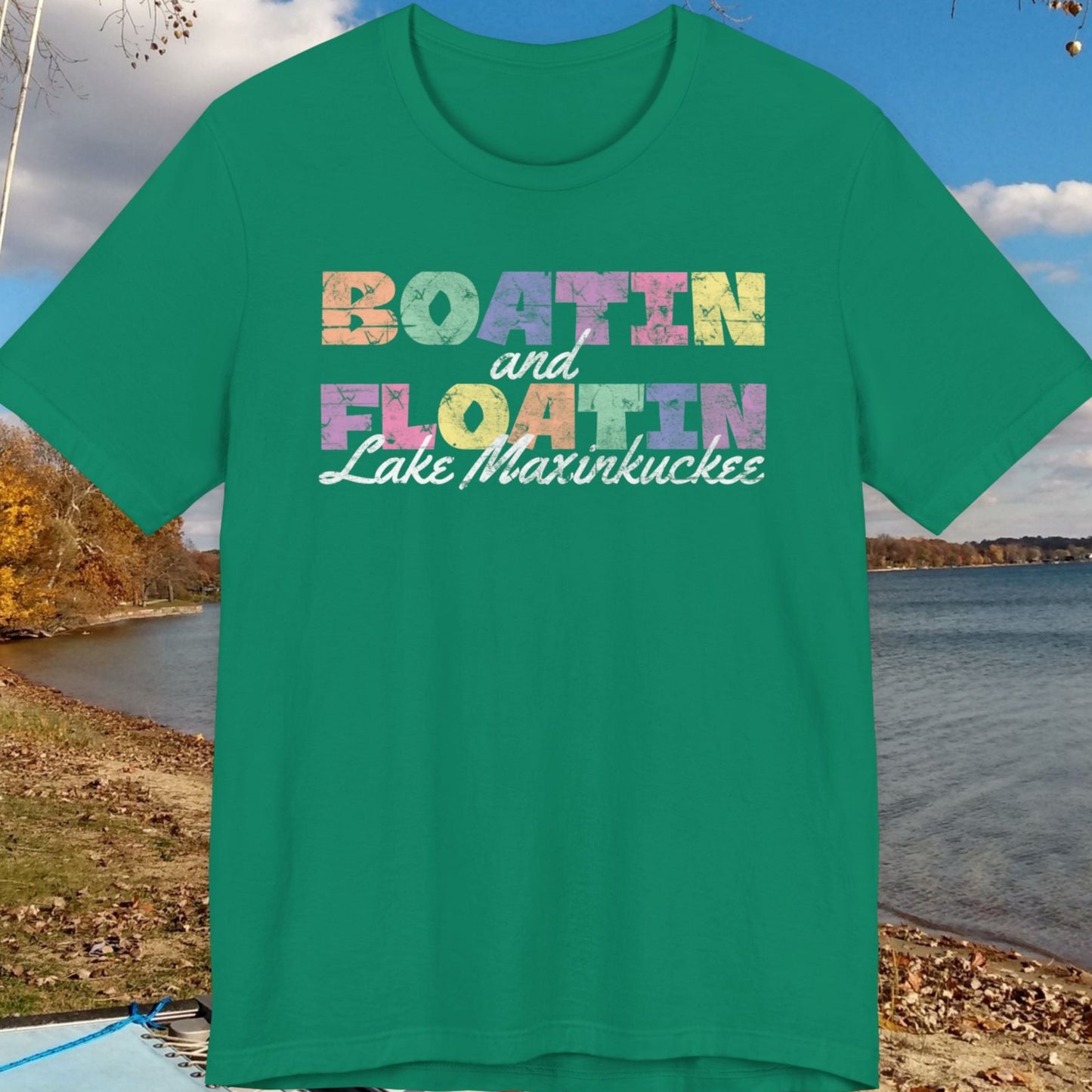 Green t-shirt with colorful BOATIN AND FLOATIN LAKE MAXINKUCKEE text on a lake shore background