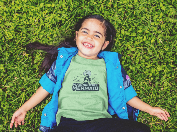 Girl laying in the grass wearing a Maxinkuckee Mermaid t-shirt