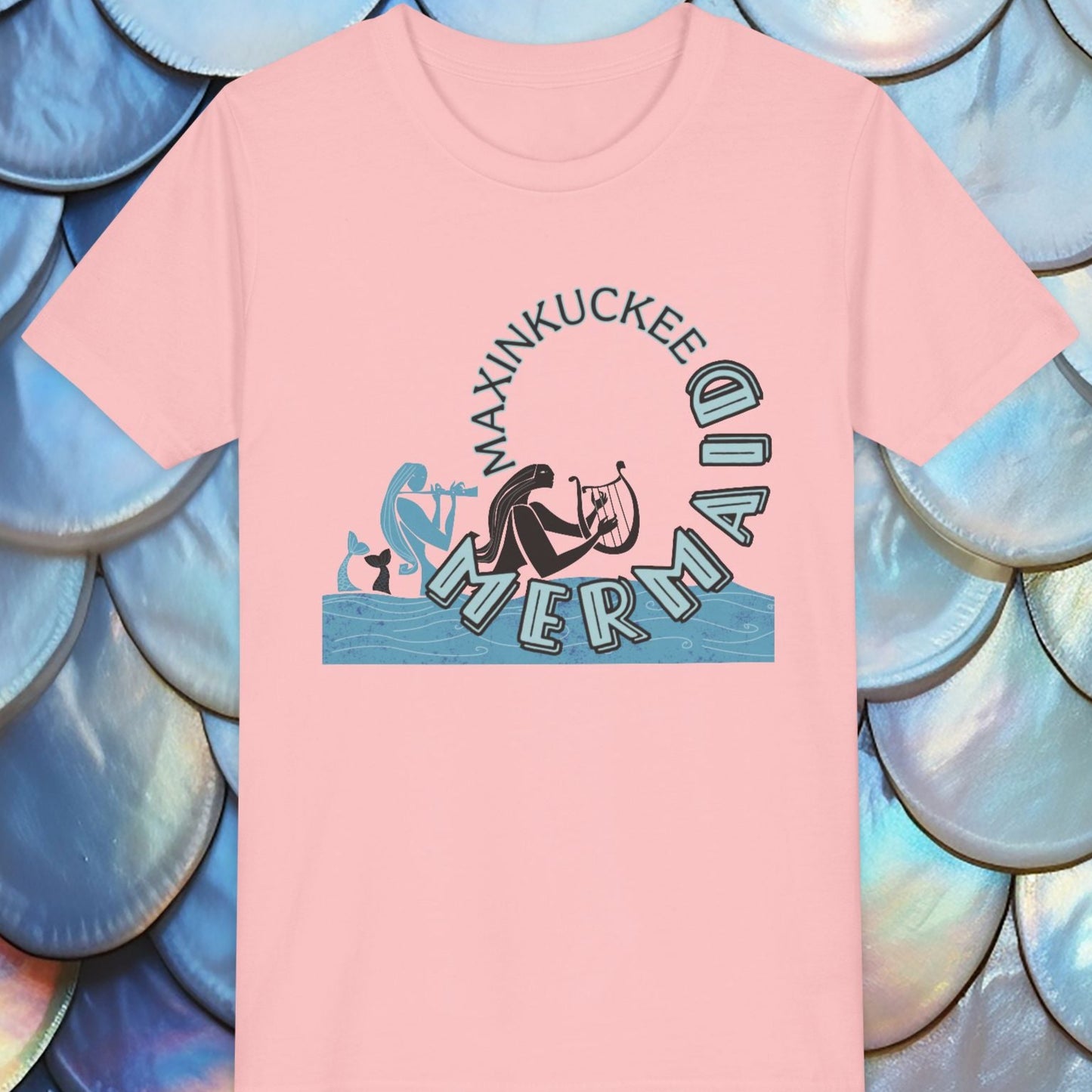 Pink t-shirt with mermaid graphic and text on a background of blue and silver scales.