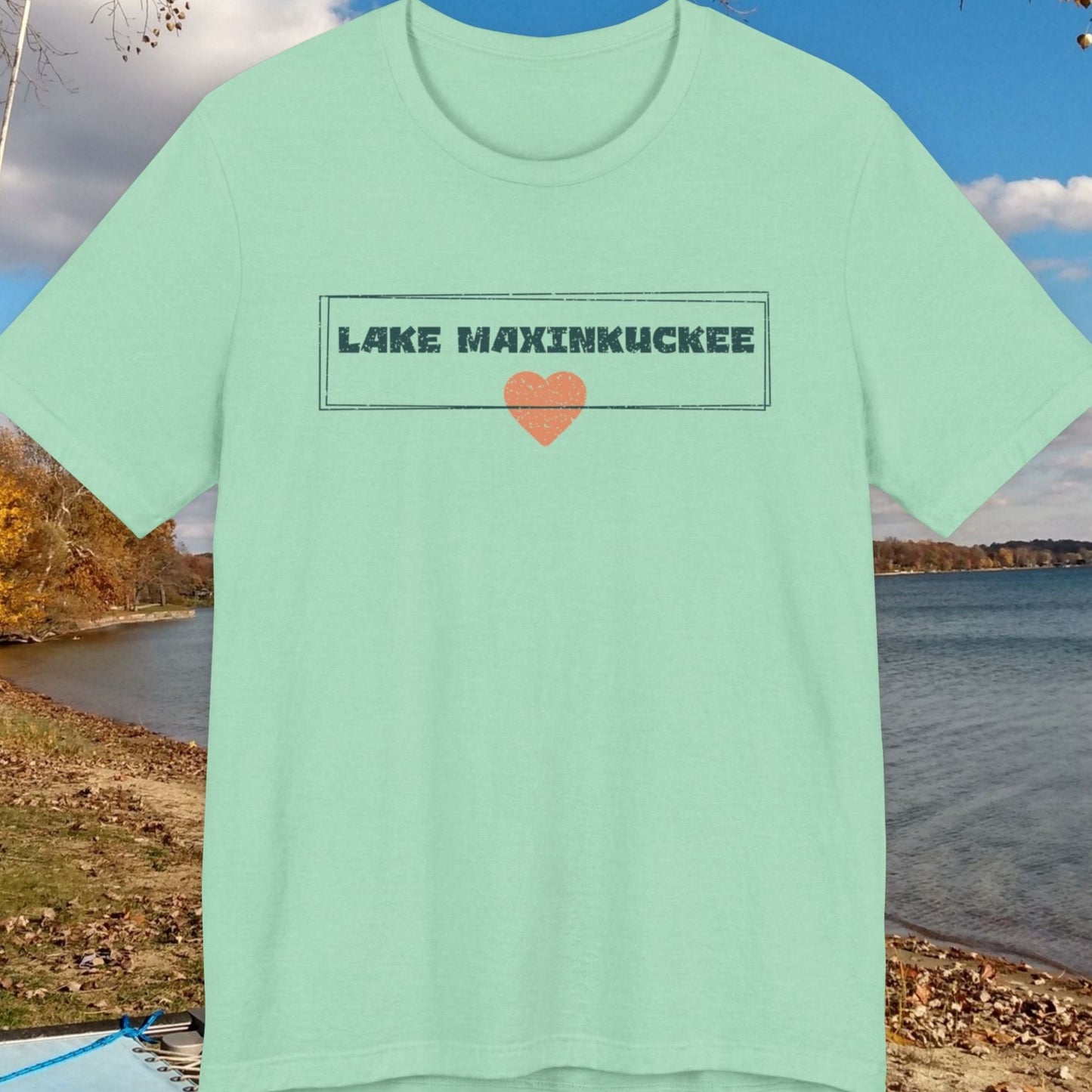 Mint green t-shirt with 'Lake Maxinkuckee' text and heart graphic on a lakeside background