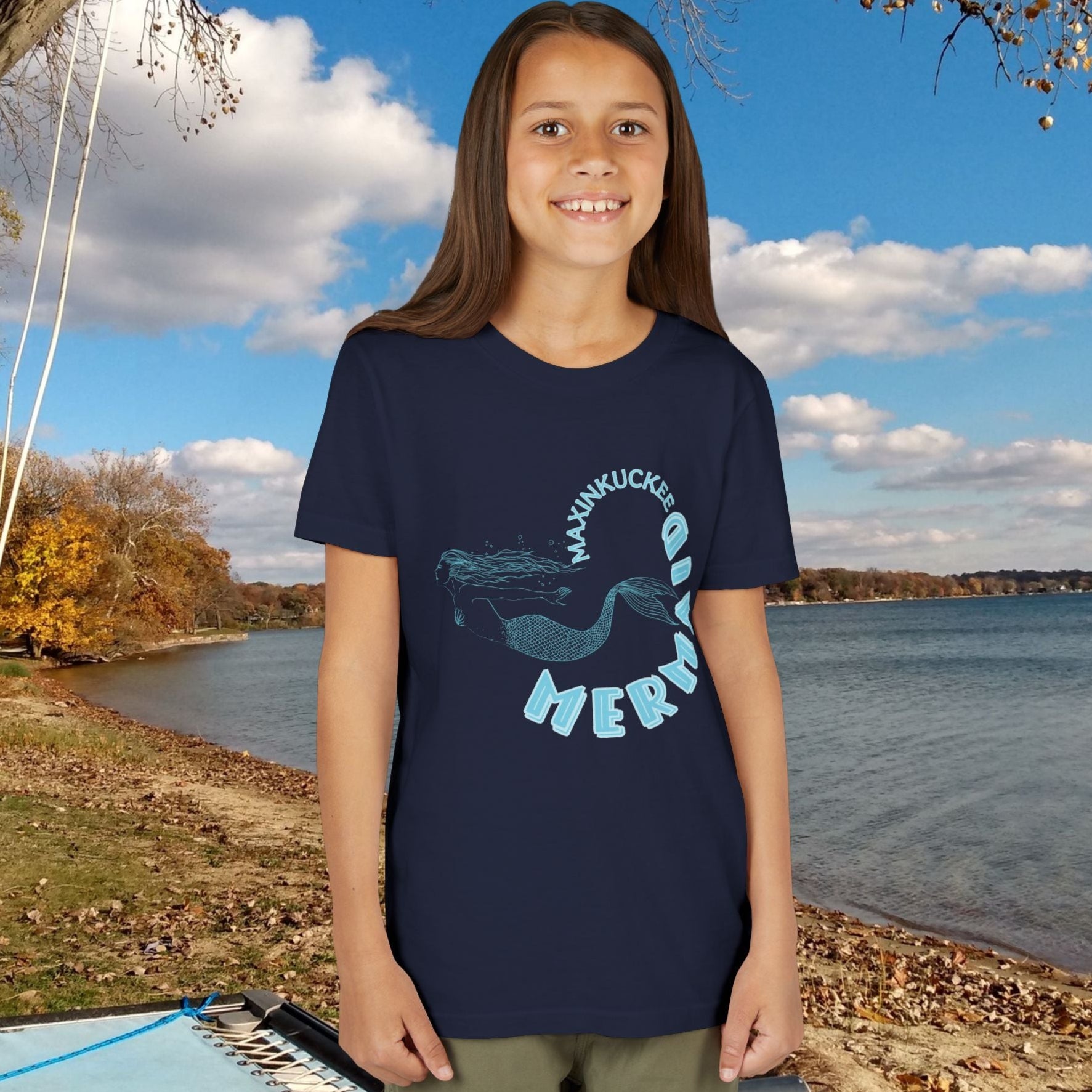 kid in a t-shirt with 'Maxinkuckee Mermaid' design on a background of blue and silver fish scales.