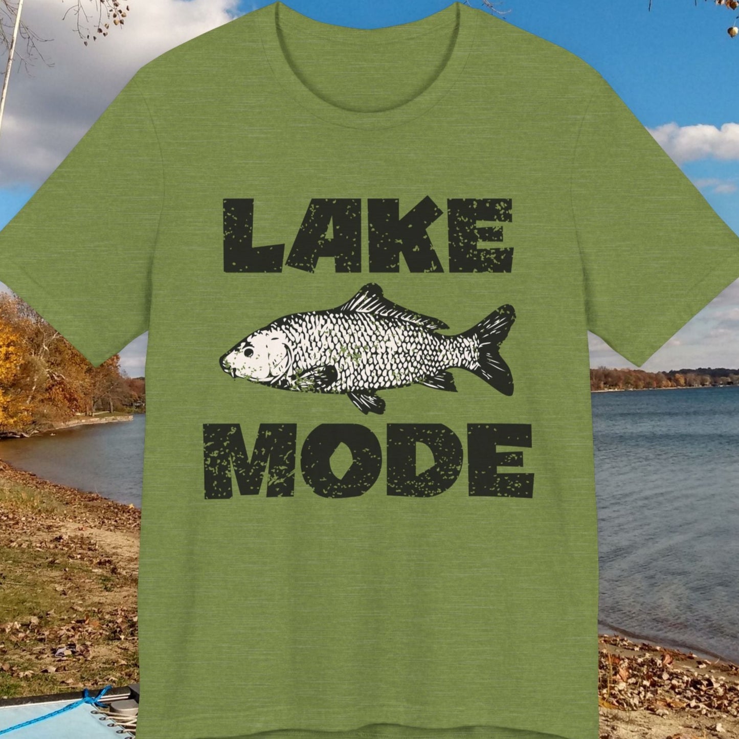 Green t-shirt with 'Lake Mode' design featuring a fish, placed outdoors by a lake.