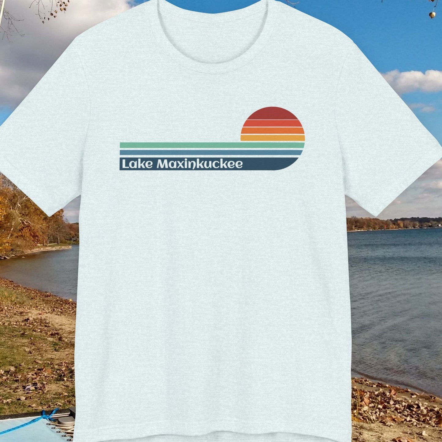 White t-shirt with 'Lake Maxinkuckee' design on a background of a lake and trees.