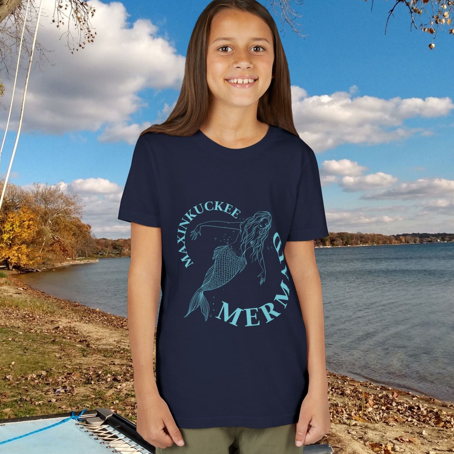 kid in a t-shirt with 'Maxinkuckee Mermaid' design on a background of blue and silver fish scales. 