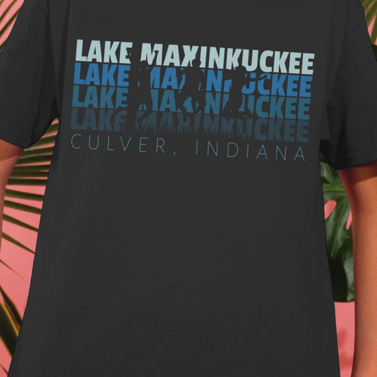 kid shirt with graphic Lake Maxinkuckee repeated 4 times horizontally from light blue to dark blue with Culver Indiana under that and an overlay of 3 jumping people in silhouette form